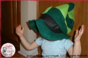 A young child, playing peekaboo, hiding her head under a big hat