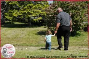 A young child, walking with an older person, holding hands