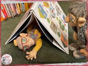 A picture of Madame Rigolotte and Maurice, two wooden puppets. Madame Rigolotte is under a picturebook, and Maurice is looking at her