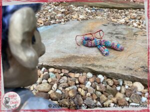 Maurice, a wooden puppet, looking at red glasses and a colorful scarf left on a path