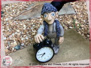 Maurice, a wooden puppet in grey tones, behind a clock