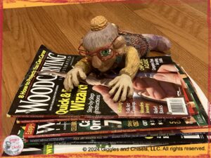 Madame Rigolotte, a wooden puppet with red glasses, on a pile of woodworking magazines