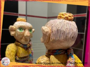 Mme Rigolotte, a colorful, wooden puppet, looking at herself in the mirror