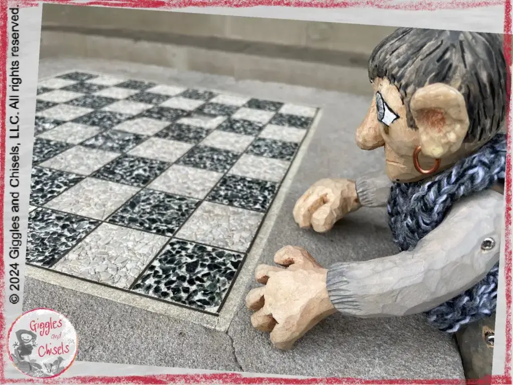 A picture of Maurice, a wooden puppet in grey shade, looking at a checker board found in a park.