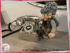 Maurice, a wooden puppet in grey colors, looking at an old phone in silver color
