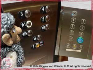 Maurice, a wooden puppet in grey colors, looking at the bottons of an elevator