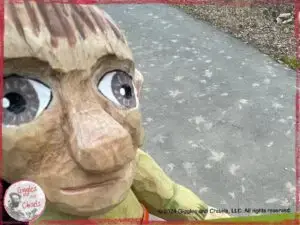 A picture of Pierre Qui Roule, a wooden puppet, in front of a pattern on the ground, made out of leave prints