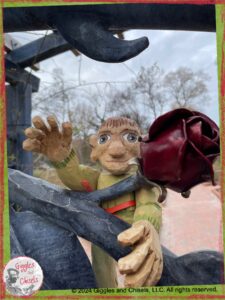 A picture of Pierre Qui Roule, a wooden puppet, behind a gate made out of metal, with the sculpture of a rose