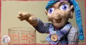 A picture of Petite Clothilde, a wooden puppet, in front of a measuring cup.