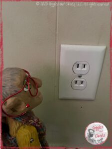 Mme Rigolotte, a wooden puppet, looking at an outlet