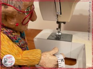 Mme Rigolotte, a wooden puppet, in front of a sewing machine