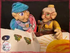Petite Clothilde and Mme Rigolotte, two wooden puppets, reading a picturebook together