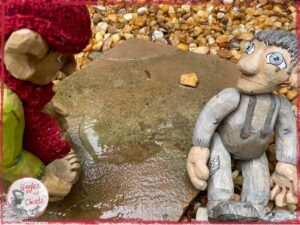 Maurice, a wooden puppet, looking at Pierre Qui Roule, another puppet who has his feet in a puddle