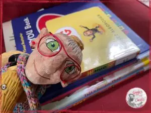 Mme Rigolotte, a wooden puppet, on the top of a pile of picturebooks