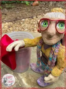 Mme Rigolotte, a wooden puppet, in front of a container with a red scarf in it
