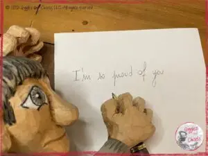 A picture of Maurice, a wooden puppet, writing "I am so proud of you" on a piece of paper