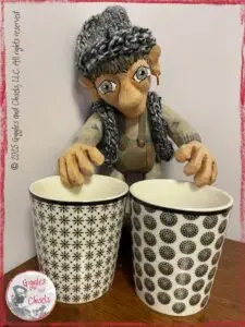 Maurice, a wooden puppet, in front of two mugs with different patterns