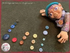 Petite Clothilde, a wooden puppet, making a graph out of buttons