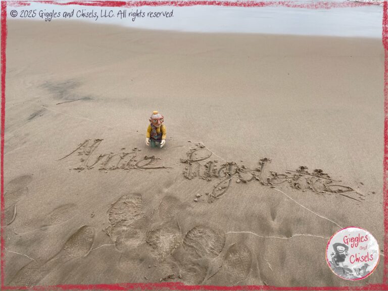 Mme Rigolotte, a wooden puppet, on a beach, with her name written in the sand