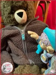 Petite Clothilde, a wooden puppet, with a teddy bear wearing a jacket with a zipper