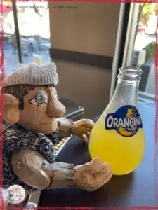 Maurice, a wooden puppet, in front of a bottle of Orangina