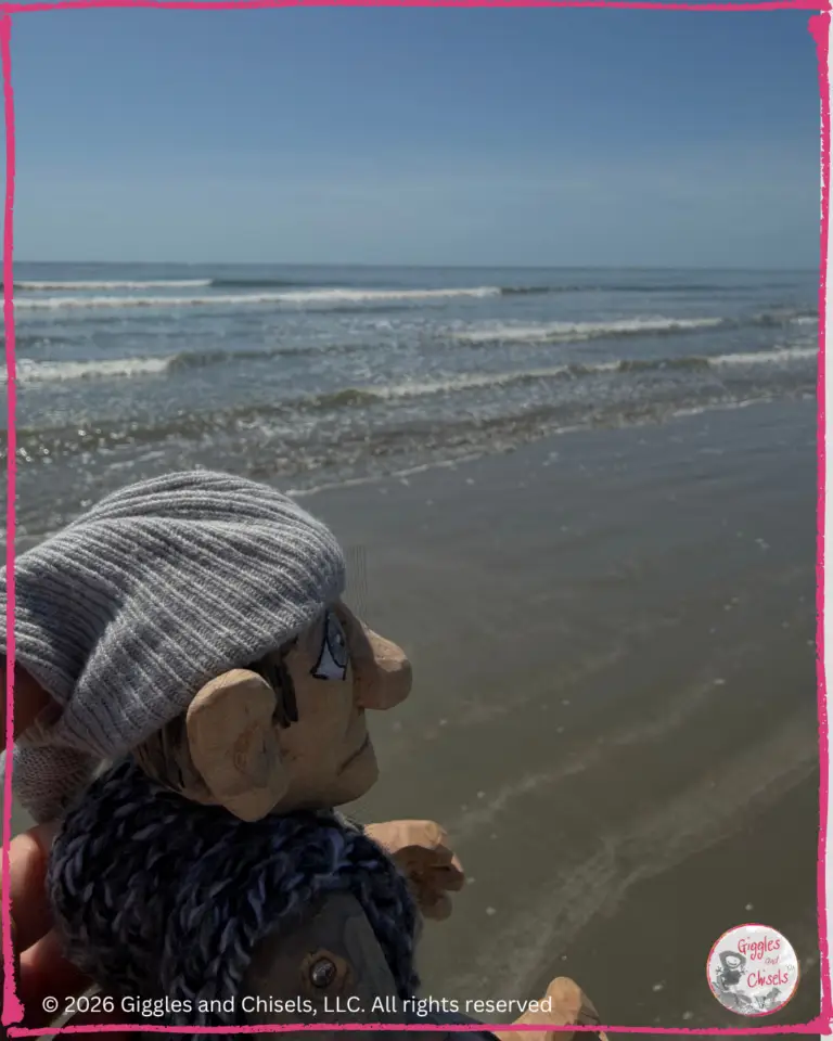 A picture of Maurice, a wooden puppet, on a beach, looking at the waves