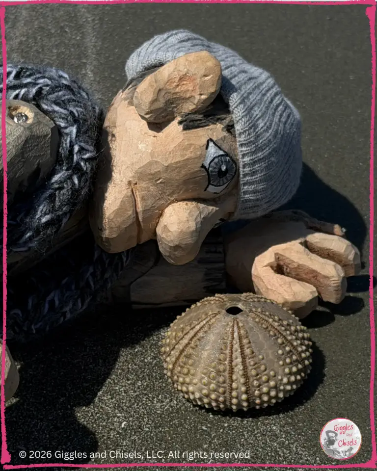 A picture of Maurice, a wooden puppet, on a beach, looking at an urchin test