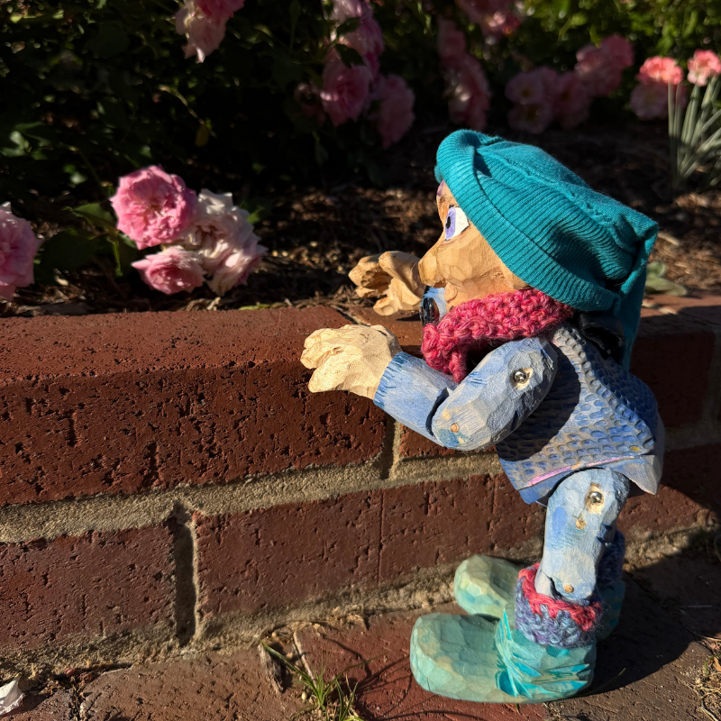 Petite Clothilde, a wooden puppet in blue colors, talking to a rose
